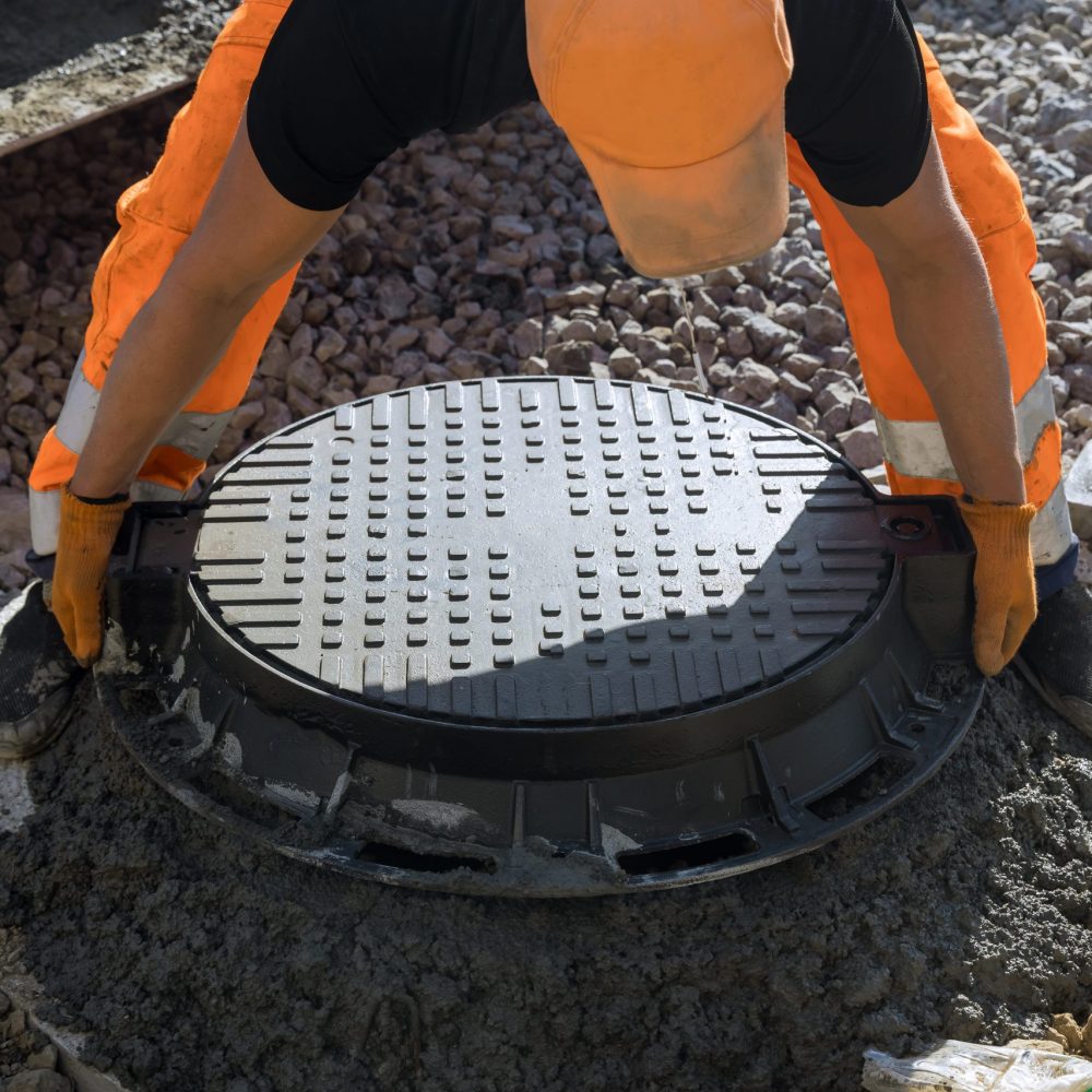Installing cast iron sewer hatch on a concrete base of installation of water main sewer well in the ground at a construction site